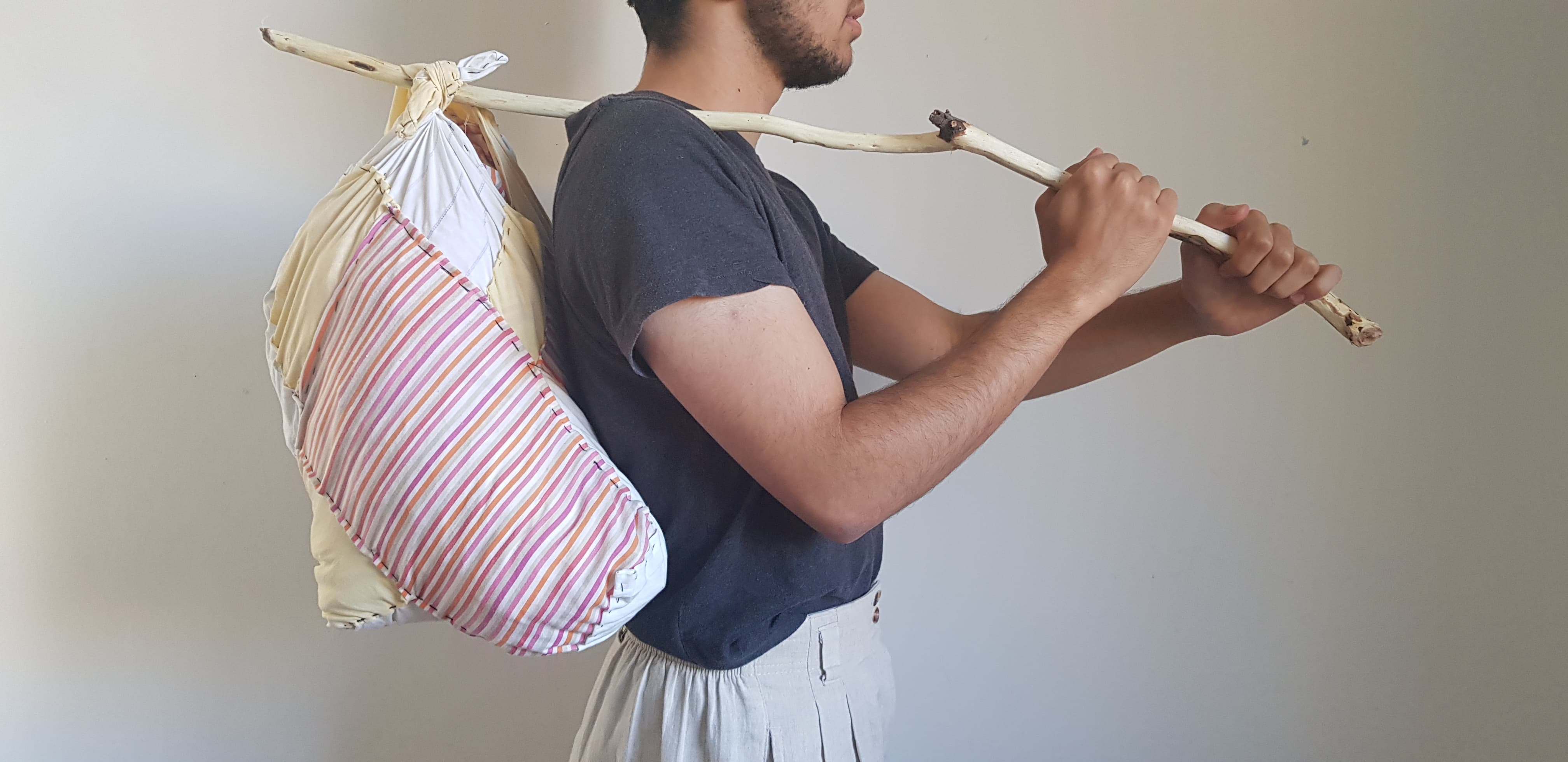  a person with stubb facing towards the right, holding a stick over their shoulder. 
                       Attached to the stick is a bag sewn from scrap fabric