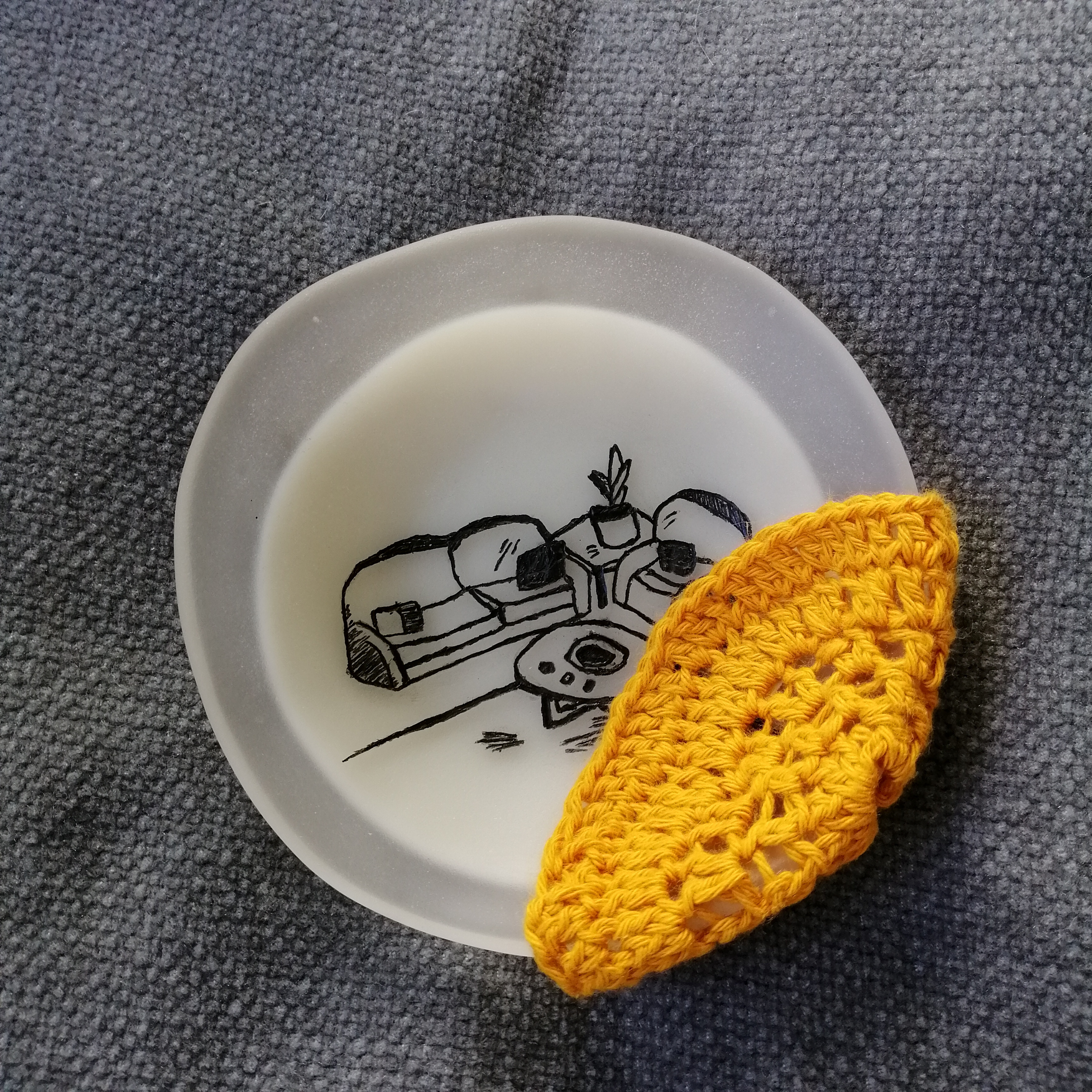 a small glass dish with a crocheted hat. The dish is colourful and has a yellow house inked into the front