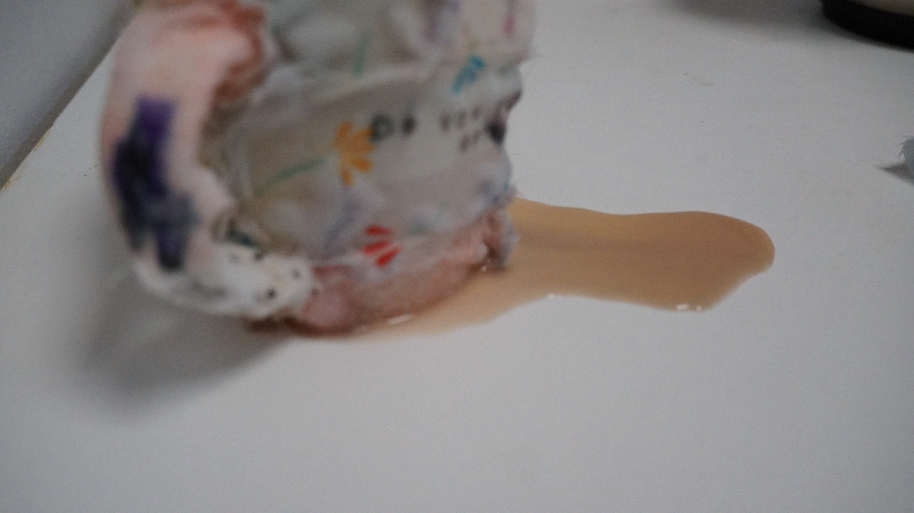 a scrap fabric covered cup (sewn) with fineliner marks. It has been filled with water and a tea spill trails across a white background. A fabric covered spoon is also in the cup
